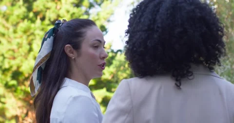 Diverse women standing in yard, left woman initiating talk wearing scarf, right Stock Footage 343100685