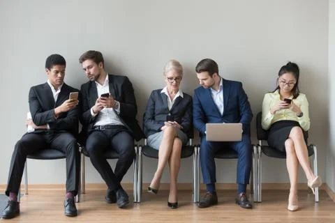 Diverse work candidates sit in queue using gadgets before interv Stock Photos