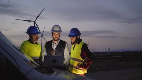 Diverse work team professional engineers using laptop at sunset wind power plant Stock Footage 256091989