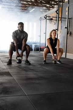 Diverse workout partners performing kettlebell squats in CrossFit gym with Stock Photos