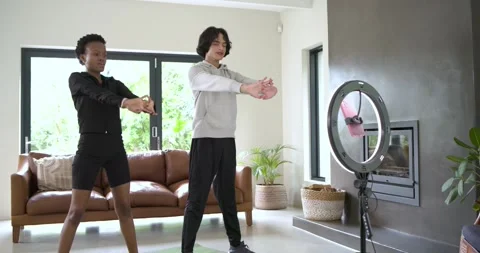 Diverse workout partners stepping onto yoga mats at home squatting and checking Stock Footage 339320782