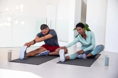 Diverse workout partners stretching hamstrings on black mats in living room with Stock Photos