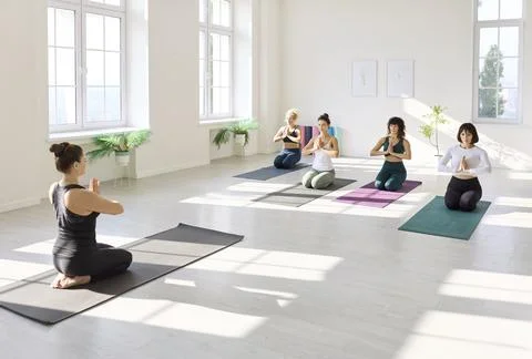 Diverse yoga class in prayer pose, guided by instructor in sunlit minimalist Stock Photos