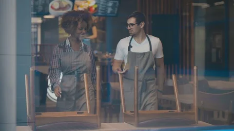 Diverse young waiting staff preparing cafe for opening arranging furniture Video stock 123437134