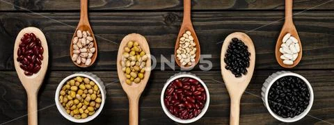 Diversity of beans inside wooden spoons. Black wood background Stock Photos