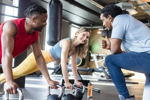 Diversity couple doing push-ups in gym with coach Stock Photos