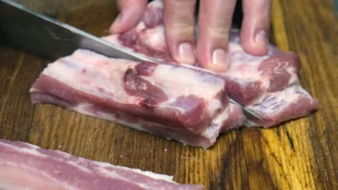 Divides raw pork ribs with a knife on a wooden board. Stock Footage 233258532