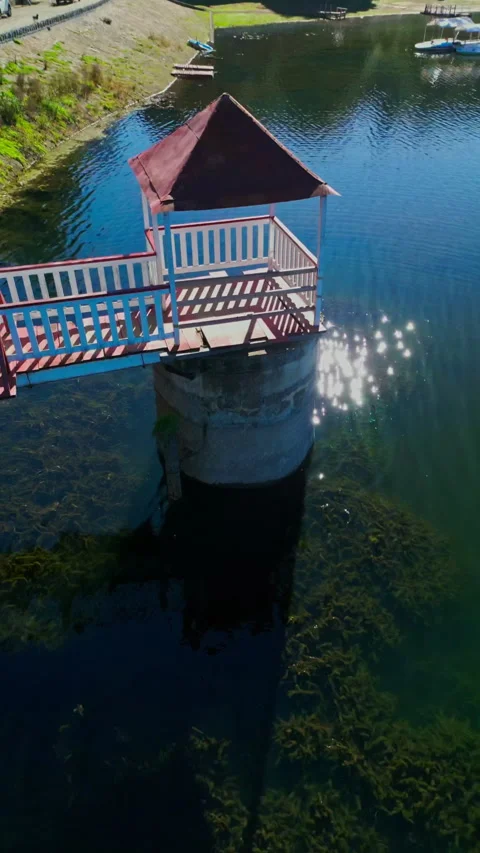 Diving aerial move down past a red-roofed gazebo bridge toward sparkling water Stock Footage 346014981