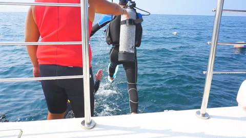 A diving instructor pushes a person in a wetsuit into the blue sea water for div Stock Footage 117517128