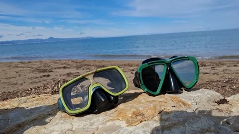 Diving masks lie abandoned on a rock with the sea in the background during .. Stock Footage 337343695