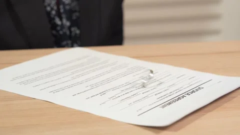 Divorce agreement on the table. A view of spinning wedding ring on the decree. Stock Footage 145992376
