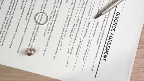 Divorce agreement on the table. A view of spinning wedding rings on the decree. Stock Footage 145992421