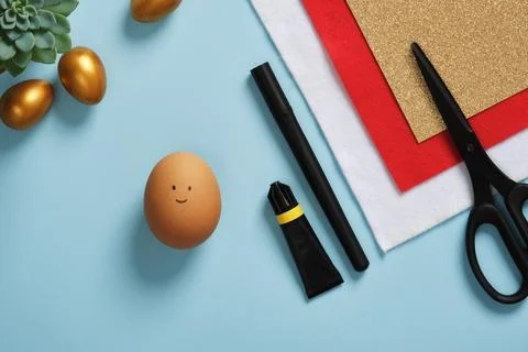 A DIY Easter egg with a smiling face on a background of art supplies. Craftin Stock Photos