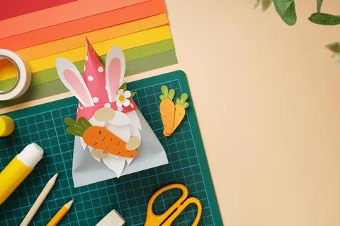 DIY Easter gnome with bunny ears holding paper carrot. Art workspace with sci Stock Photos
