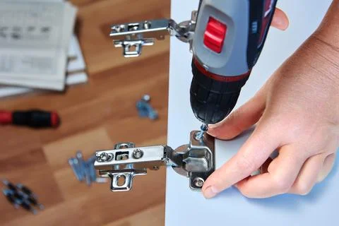 DIY installation adjustable door hinges on cabinet of flat pack, using powe.. Stock Photos