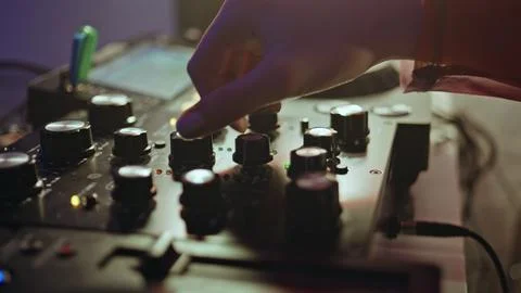 DJ hand tweaking knobs on mixer mixing music in clubbing scene closeup. Stock Photos