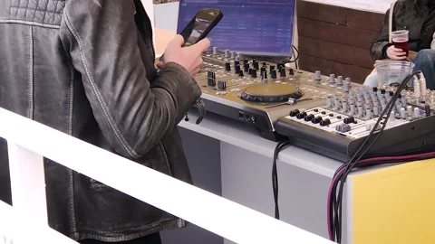DJ in a leather jacket plays music behind deck mixes tracks and surfs smartphone 스톡 동영상 249350147