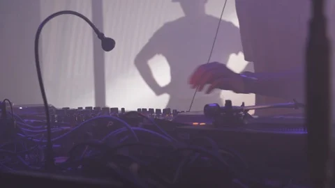 DJ playing vinyl records behind a turn table in a techno night club Stock Footage 117877645