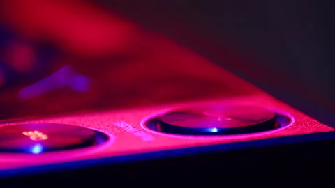 DJ presses start buttons on mixer and starts music in nightclub lit by neon Stock Footage 187051958