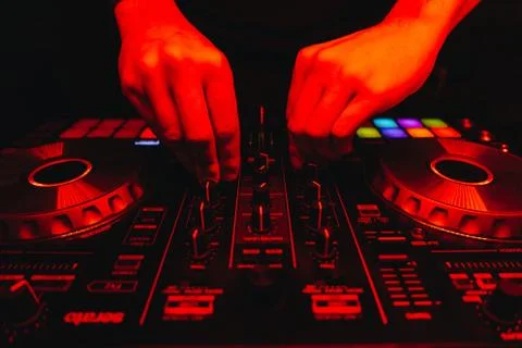 DJ is turning switches on controller close up in red nightclub light, male ha Stock Photos