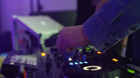 DJ turns buttons on mixing console illuminated by neon lights in the nightclub Stock Footage 219667676