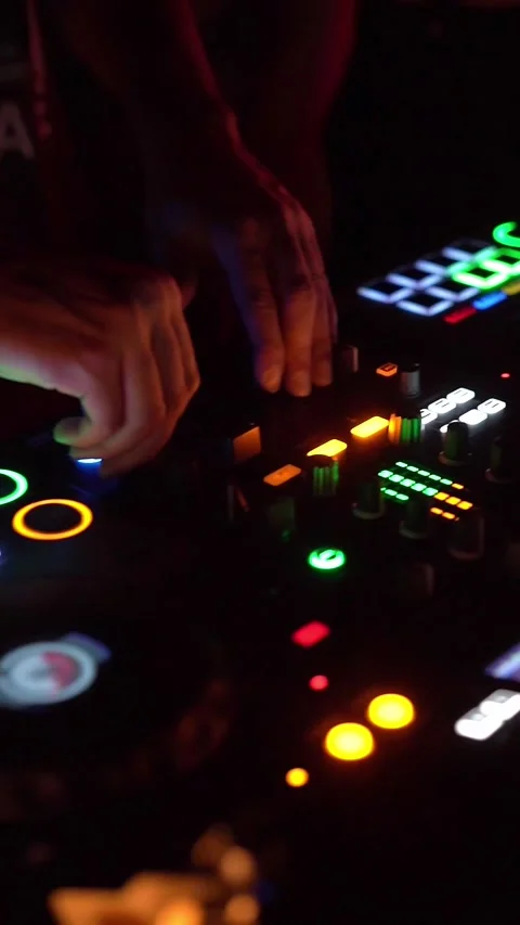 A DJ is using a mixer to blend music under vibrant lights in a nightclub Stock Footage 293760246