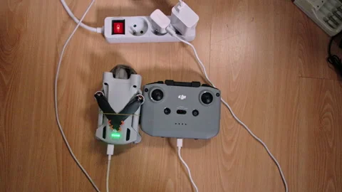 DJI Mini 3 Pro drone and RC controller charging on laminate floor. Vídeos de archivo 327560593