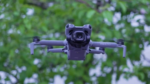 DJI Mini 5 Pro Drone hovering near green trees close-up Stock Footage 337630507