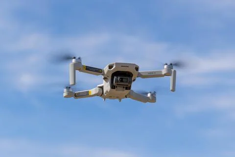 DJI Mini drone flying in blue sky with blurred propellers Stock Photos
