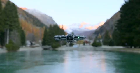 A DJI Neo 2 drone is captured hovering steadily over a serene mountain lake. Stock Footage 336774813