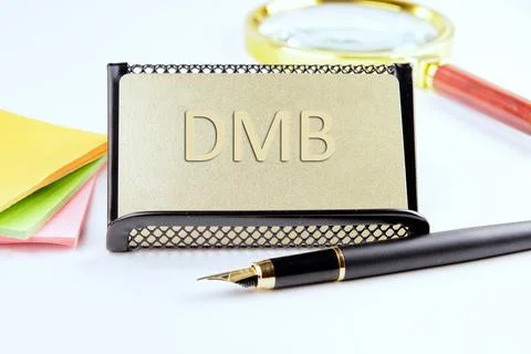 DMB text on a gold plastic card with convex text next to office supplies on.. Stock Photos