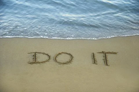 Do it written in the sand on the beach with the sea washing up the shore Stock Photos