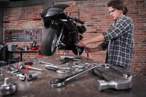 Do it yourself, young man repairing a motorcycle in the garage with red brick Stock Photos