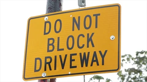 Do not block driveway yellow black rectangle sign on post outside exterior Stock Footage 251356221