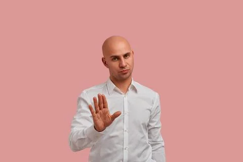 Do not do this. Serious bald man with bristle keeps palm in stop gesture, ask Stock Photos