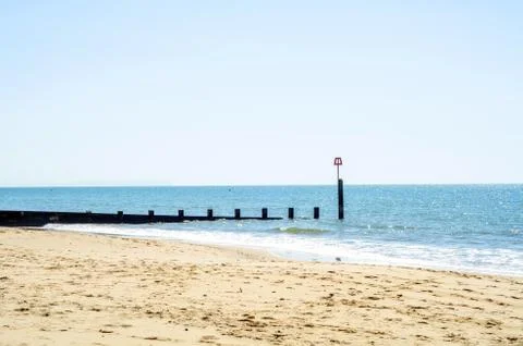 Dock pilings on a sandy beach, blue ocean and yellow sand, sunny hot day Stock Photos
