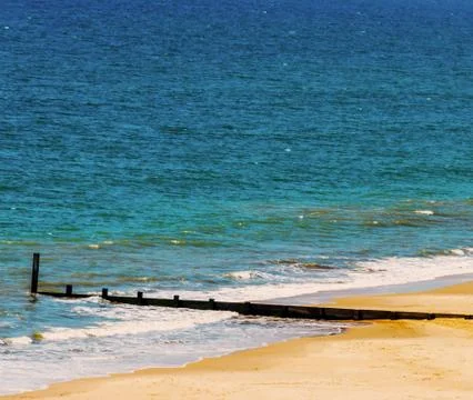 Dock pilings on a sandy beach, blue ocean and yellow sand, sunny hot day Stock Photos