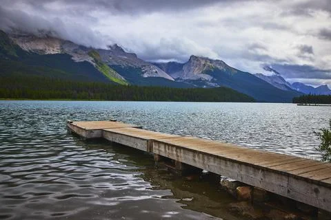Dock on Tranquil Lake with Mountain View and Forest Under Cloudy Sky Foto stock