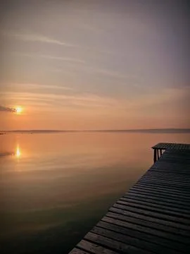 A dock is on the water with a sunset in the background Stock Photos