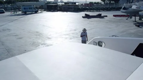 Dock Worker on White Yacht Hull at Sunlit Boatyard, Wide Establishing Shot Stock Footage 340333081