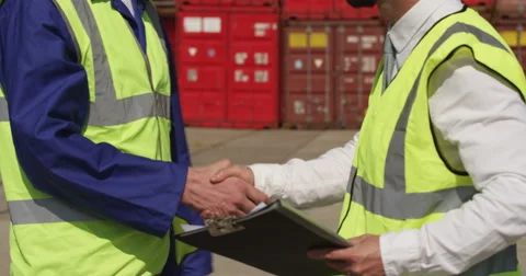 Dock workers shake hands and discuss shipping logistics in a shipyard. Stock Footage