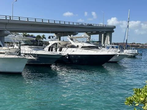 Docked yachts float in clear turquoise water near a bridge on a sunny day. Stock Photos