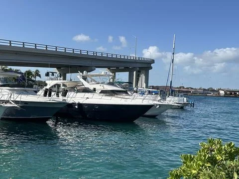 Docked yachts float in clear turquoise water near a bridge on a sunny day. Stock Photos