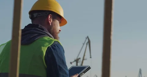 A Dockworker With A Beard In A Yellow Helmet, Works With A Tablet PC In The Port Stock Footage 121660629