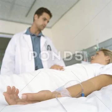 Doctor And Female Patient Lying In Hospital Bed