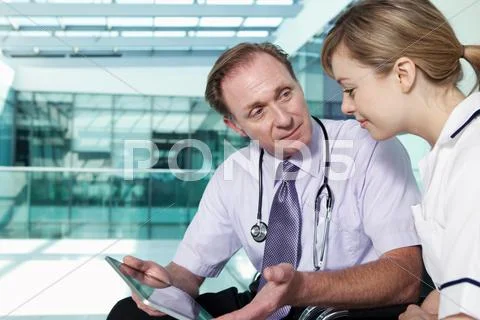 Doctor And Nurse With Medical Records On Digital Tablet