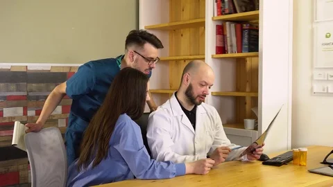 A doctor and two interns examining a patient's X-rays sitting at a table in Stock Footage 75683084