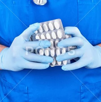 Doctor in blue uniform and sterile gloves holding white pills in pack Stock Photos