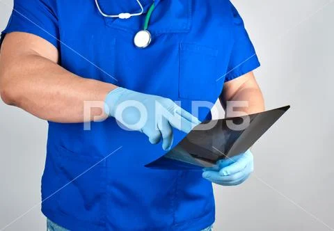 Doctor in blue uniform and sterile latex gloves holds and examines X-ray Stock Photos