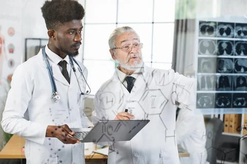 Doctor checking x ray scan while assistant using laptop Stock Photos